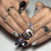 Almond press-on nails in black, white and silver-grey worn on both hands, with stars, sparkle and a small black figure