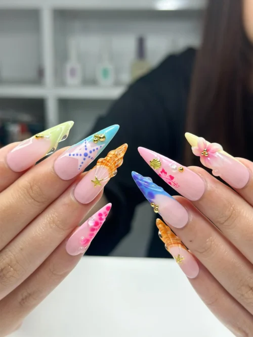 Side view of pink stiletto press-on nails with colourful seashell tips, a starfish and tiny gold charms, hands held out