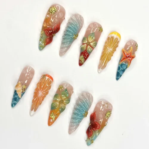 Sheer pink stiletto press-on nails laid flat with a 3D lemon and orange slice, a teal fan, hibiscus and a starfish