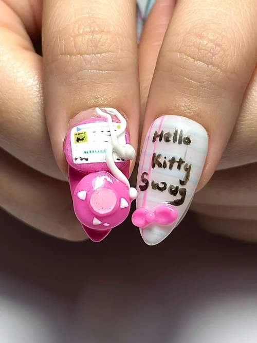 Close-up of two press-on nails: a pink 3D game console with a white cable beside a white nail with black script lettering