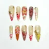 Sheer cream stiletto press on nails with 3D pink lilies, a burgundy chrome spiral, striped tips, gold beads and gems