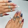 Almond press-on nails worn on two hands with silver rings: red polka dots, navy and red pinstripes, a red bow and a tiny flag