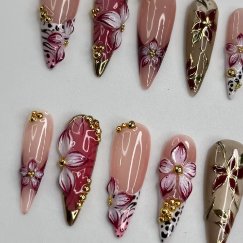 Peach, burgundy and taupe press-on nails laid flat, showing white 3D flowers, gold beads and leopard-spot tips