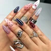 Close view of navy, pink and red almond press-on nails worn on a hand, with dotted, striped and bow designs plus silver rings