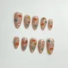 Ten sheer nude almond press-on nails laid flat on white, each with tiny sculpted 3D fish in orange, teal, yellow and white