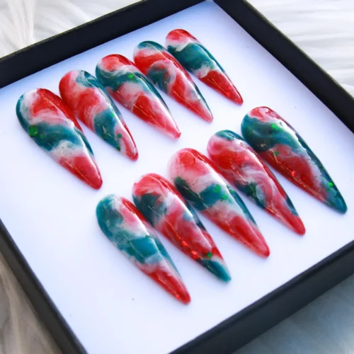 Ten red, teal and white marbled stiletto press-on nails in a black box, with fine glitter flecks, seen from above