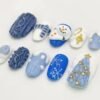 Short oval blue and white press-on nails with 3D cable knit, a snowman face, a striped scarf, a snowflake and a gem tree