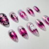 Angled view of magenta and lilac chrome almond press-on nails with a white ghost, black bats, a crescent moon and yin-yang