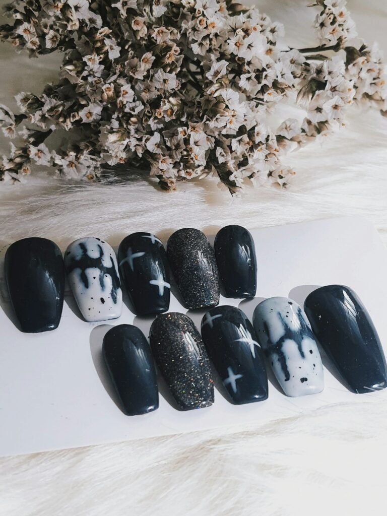 Hand-painted black and grey press-on nails with glitter and star details on a card