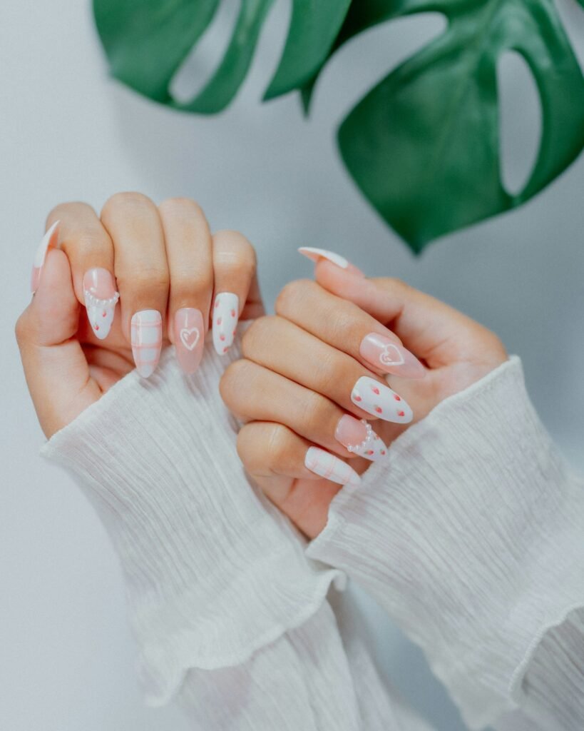 Two hands showing white press-on nails with pink hearts and pearls