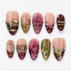 Blush olive press-on nails with burgundy accents, sculpted gold lines, leafy details, a floral motif and jeweled accents.