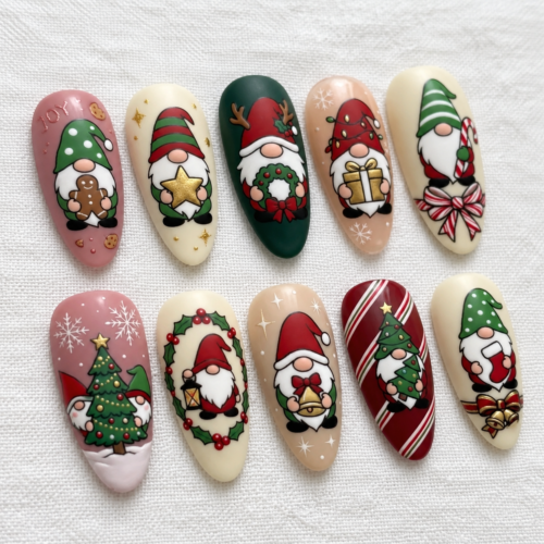 Angled view of Christmas gnome press-on nails featuring red and green hats, gold accents, and festive details on white linen.