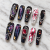 midnight nebula press-on nails with starry black tips, blue-magenta swirls, gold flecks, silver chains and red gems