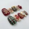 Angled view of short rounded press-on nails with gingerbread men, a candy cane, red-and-green plaid and a gold 3D bow