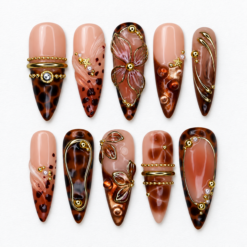 Mocha tortoiseshell press-on nails with nude blush bases, gold-tone lines, leaf accents and jewel-like details.