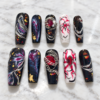 midnight nebula press-on nails with starry black tips, blue-magenta swirls, gold flecks, silver chains and red gems