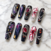 midnight nebula press-on nails with starry black tips, blue-magenta swirls, gold flecks, silver chains and red gems
