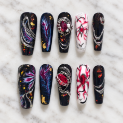 midnight nebula press-on nails with starry black tips, blue-magenta swirls, gold flecks, silver chains and red gems