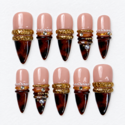 Nude burgundy band press-on nails with raised gold-tone details, pearl-like beads and glossy dark tips.