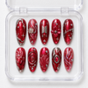 Ruby red fan press-on nails with glitter, silver ornamental lines, stars, a flower, bow and shell-inspired details.